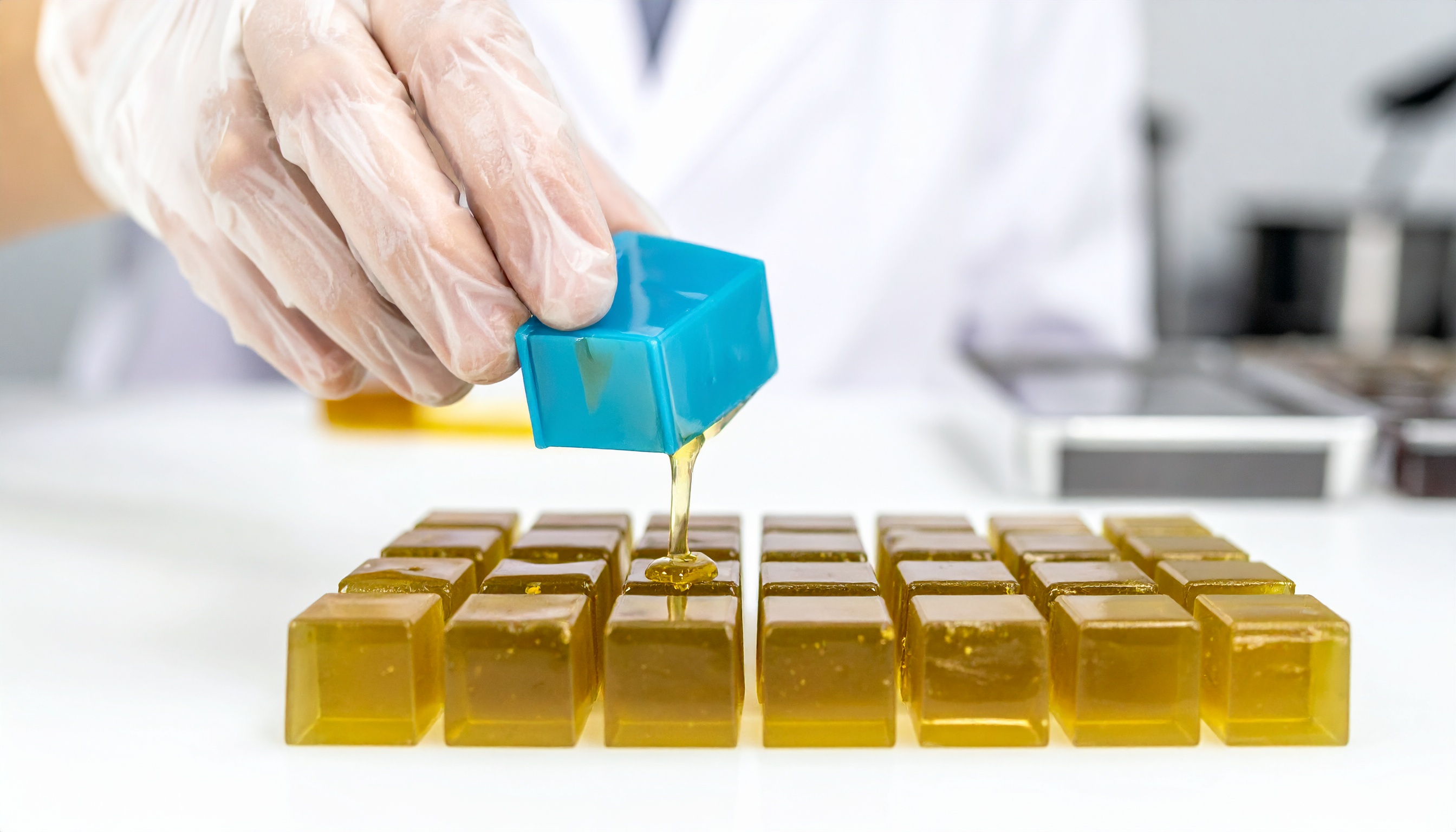 hands wearing food safe gloves carefully pouring liquid into cube shaped gummy m - Steve's Goods