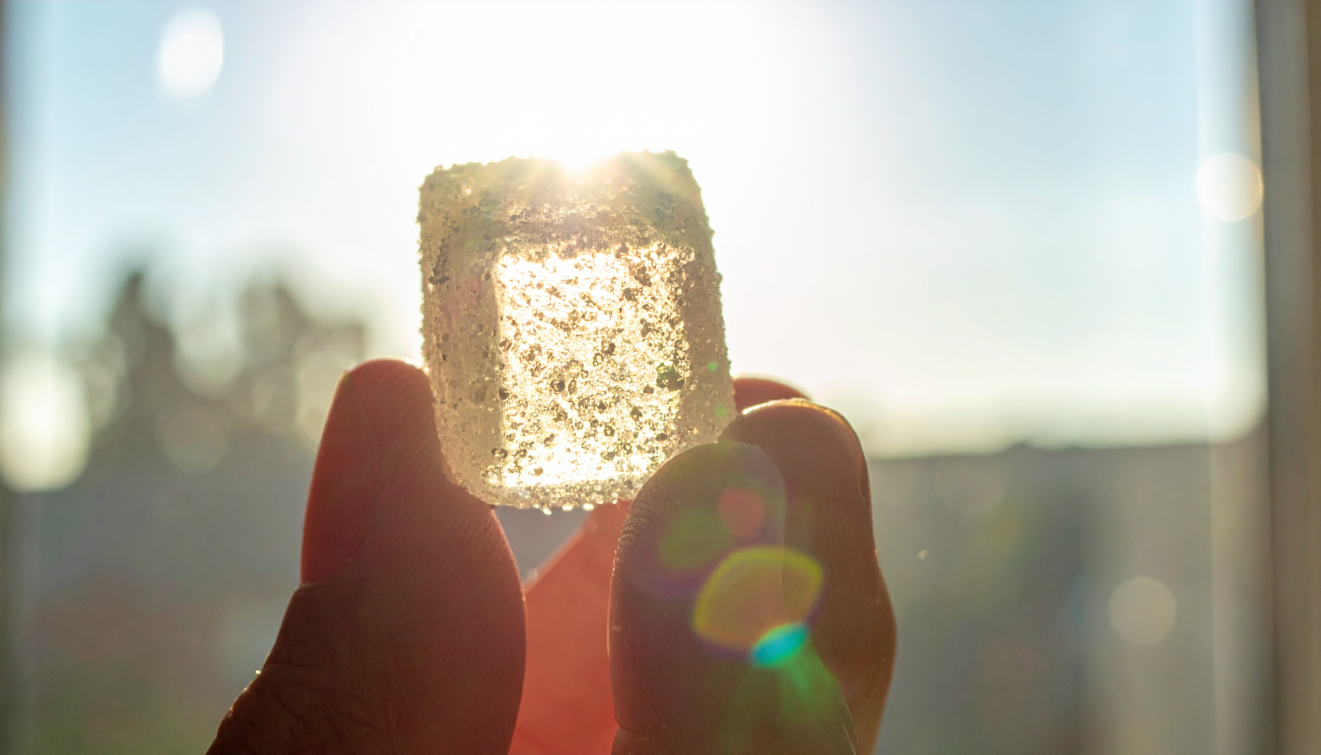 single cube shaped sugar coated translucent gummy held between fingers against a sunl - Steve's Goods CBD