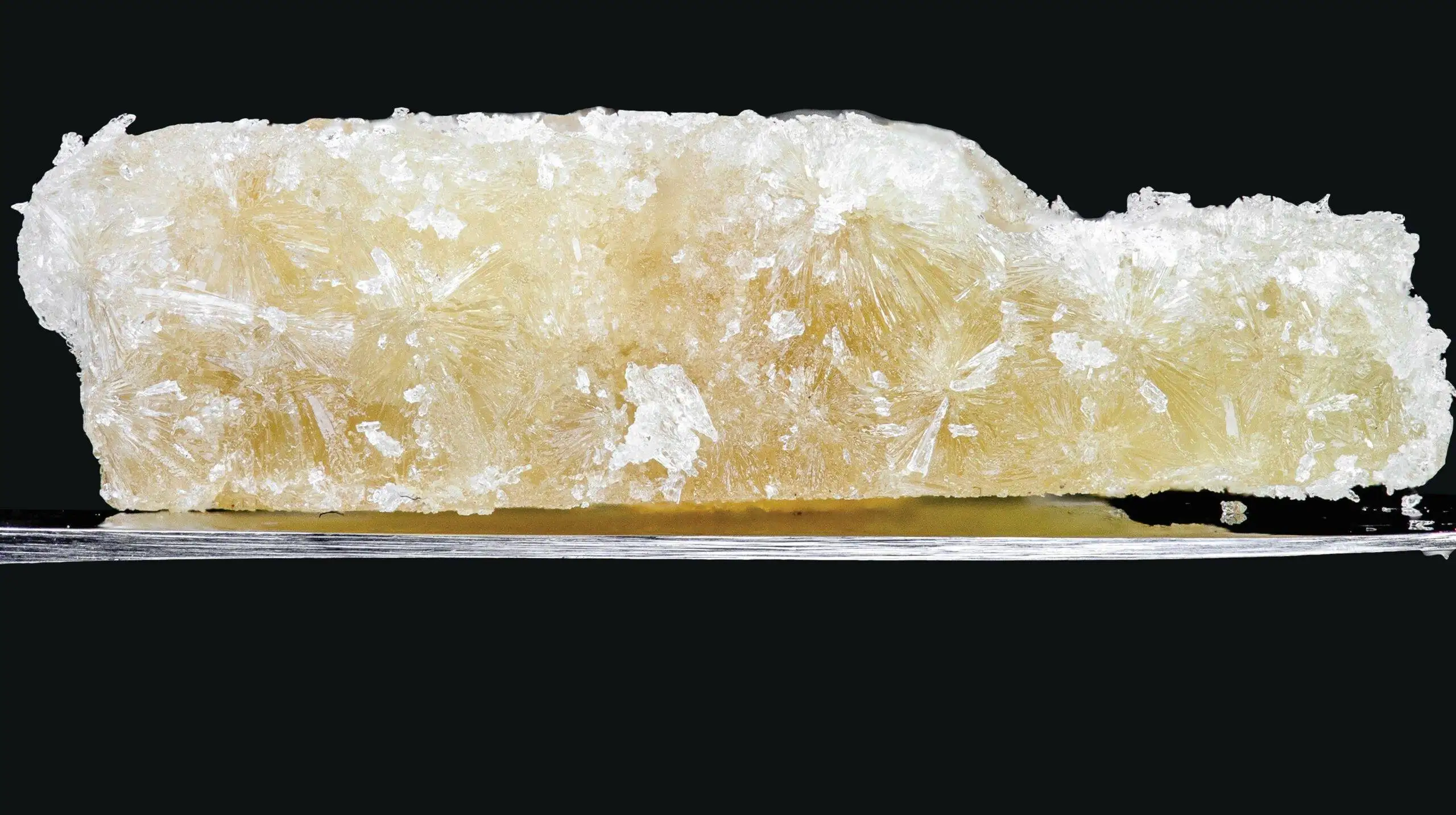A piece of white crystal, reminiscent of cbd dabs, resting on a stark black background.